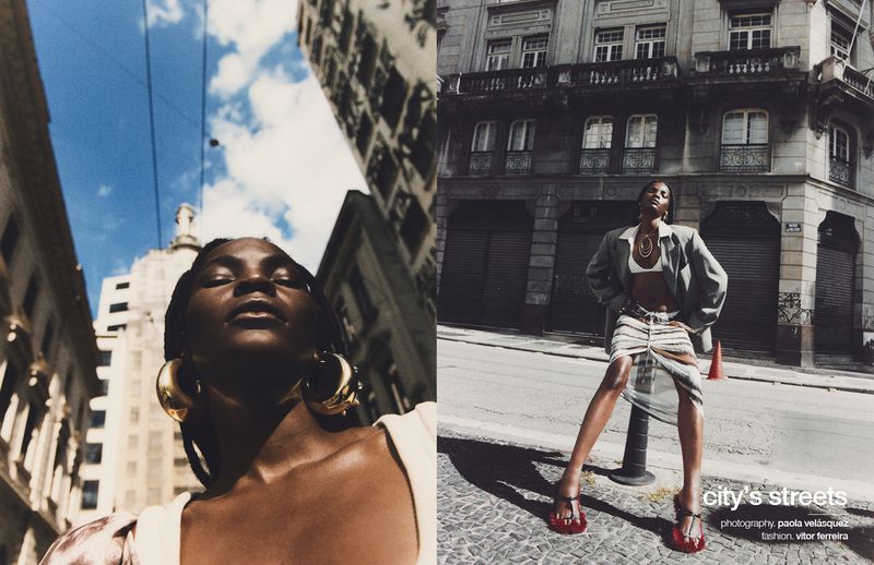 Fashion editorial featuring an African-American woman posing in an urban street, wearing a skirt and blazer, buildings and sky visible.