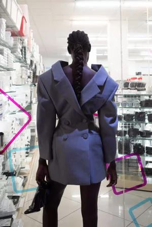 Model standing with back to camera wearing a grey structured blazer dress inside a retail store