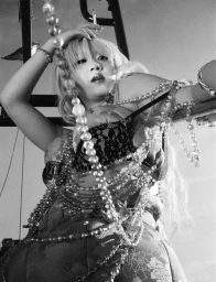 Black and white editorial portrait of a woman draped in long crystal beaded necklaces wearing a lace bra