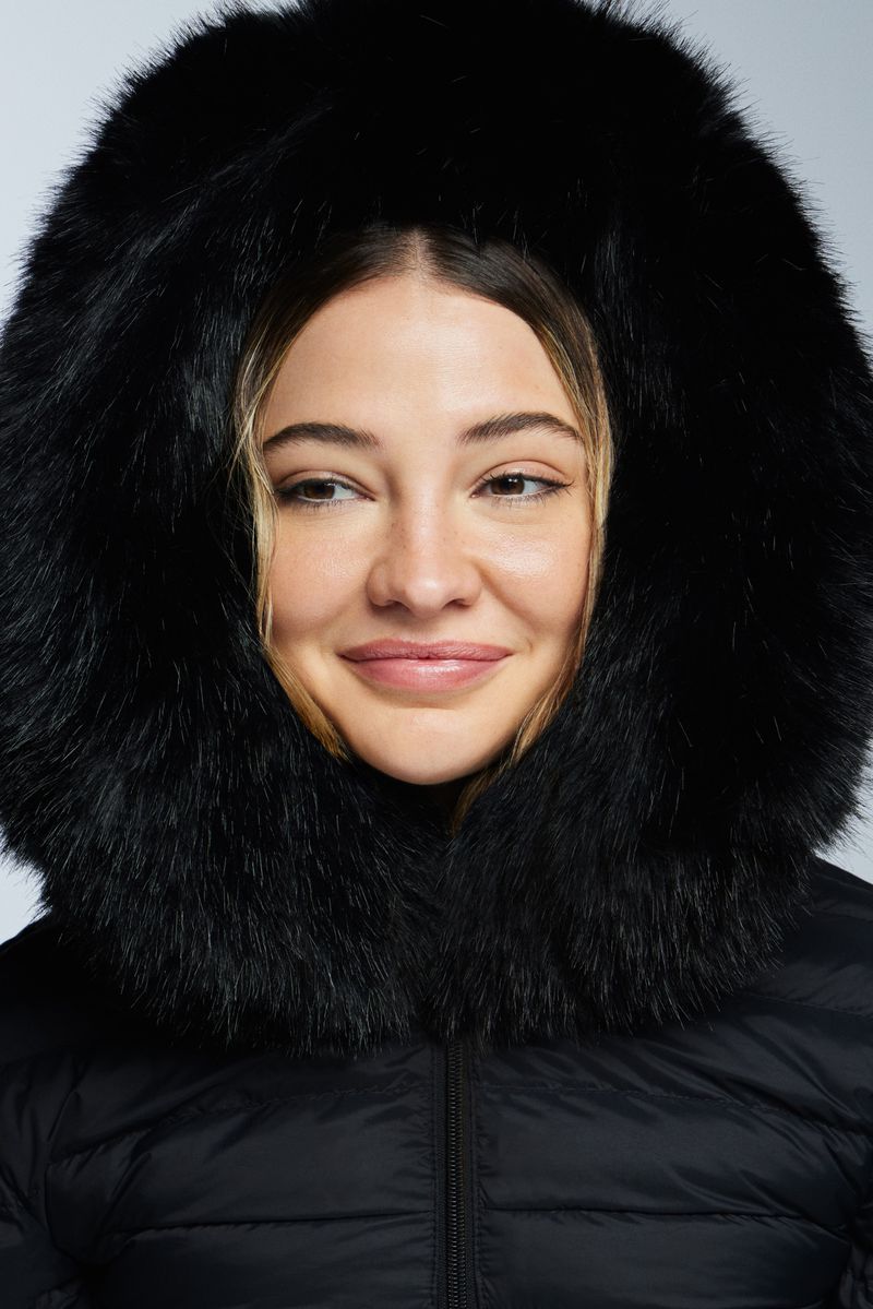 Close-up studio portrait of a smiling adult woman wearing a black puffer coat with a large faux-fur hood. Beauty and Fashion.