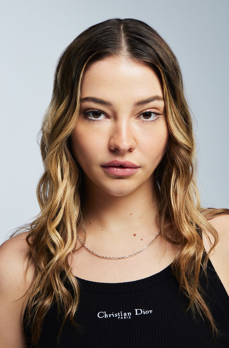 Portrait of adult female with wavy brown-blonde hair wearing a black tank top in a light studio setting with soft lighting.