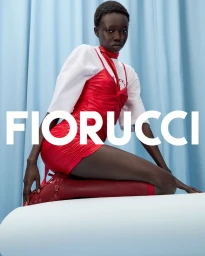 Black model in red slip dress and white t-shirt kneeling on white surface against blue draped curtain for Fiorucci SS25