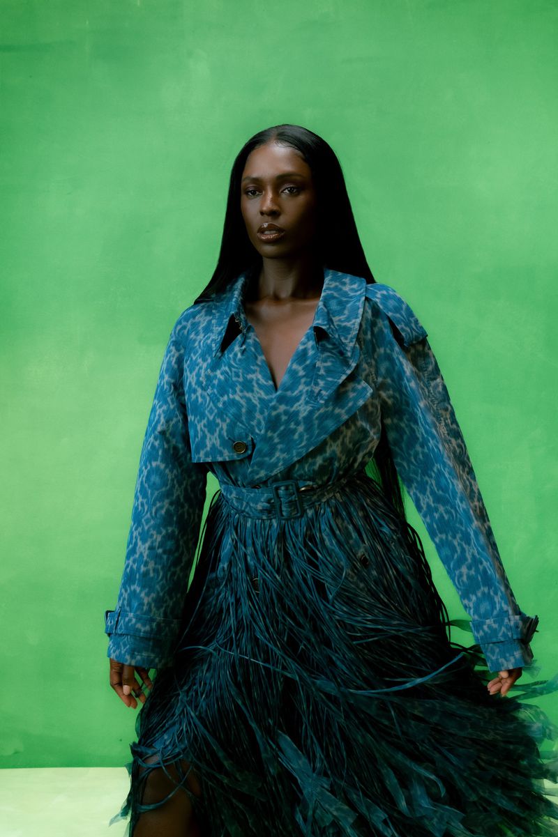 Elegant Black woman in an animal-print blazer and teal feather skirt poses against a lime-green backdrop in a fashion studio shot.