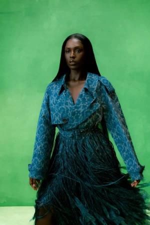 Elegant Black woman in an animal-print blazer and teal feather skirt poses against a lime-green backdrop in a fashion studio shot.
