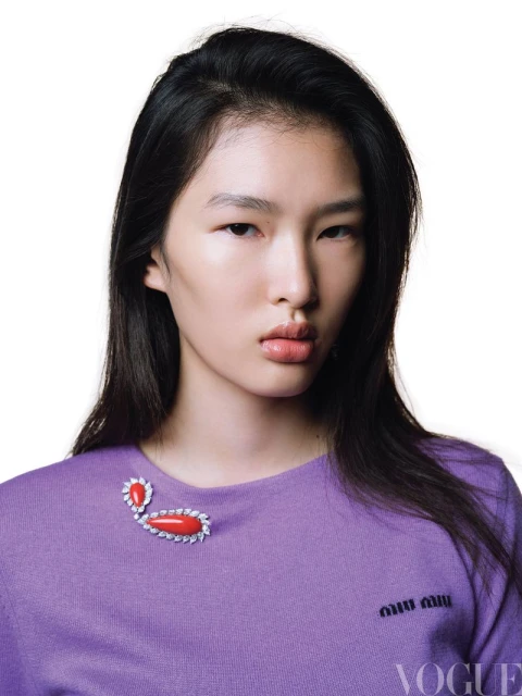 Close-up studio shot of a young Asian woman with dark hair and fair skin wearing a lilac sweater with a decorative brooch.