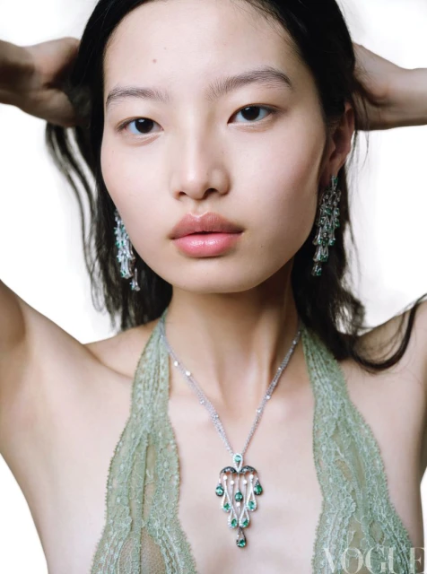 Close-up shot of an Asian woman wearing dangling jewelry, and a green halter top with a Vogue logo in the lower right corner.