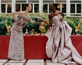 Two female models in high-end evening gowns standing by an outdoor banquet table clinking glasses for Vogue China.