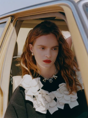 Portrait of a red-haired woman with fair skin in the passenger seat of a car wearing a Chanel necklace and sweater.
