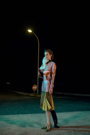 Elegant woman with fur stole posing at night near a street lamp in a stylish dress with green heels on an empty road.