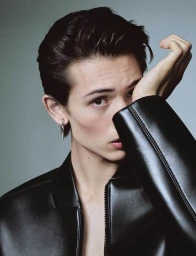 Close-up portrait of a young male model wearing a black leather jacket against a neutral grey studio background