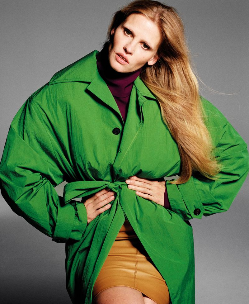 A female model poses in an oversized bright green trench coat against a gray background.