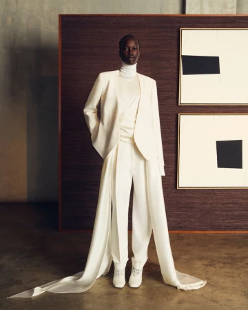 Elegant African-American woman in a white suit, with a white turtleneck and long white tails on the trousers, posing in a studio.