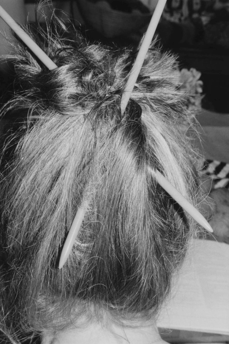 Close-up, black and white shot of person's hair styled in an updo with several hair sticks inserted, creating a textured, intentional look.