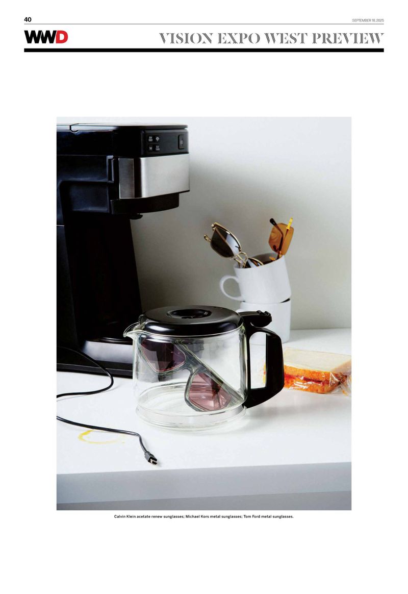 Still life features a coffee maker, coffee pot with sunglasses inside, two coffee cups, and a sandwich on a white surface.