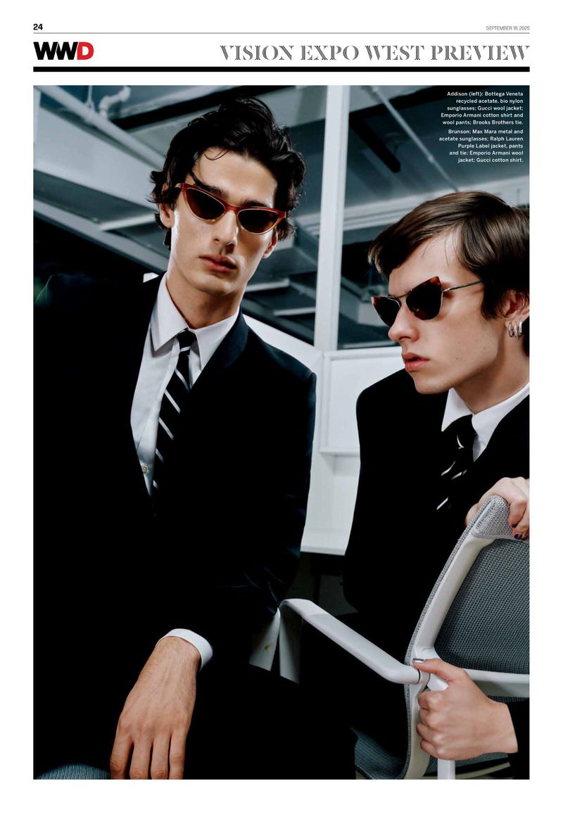 Two adult males in black suits and ties pose indoors wearing red cat-eye sunglasses, showcasing fashion editorial style and eyewear.