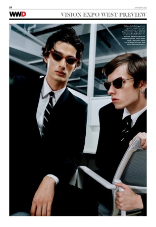 Two adult males in black suits and ties pose indoors wearing red cat-eye sunglasses, showcasing fashion editorial style and eyewear.