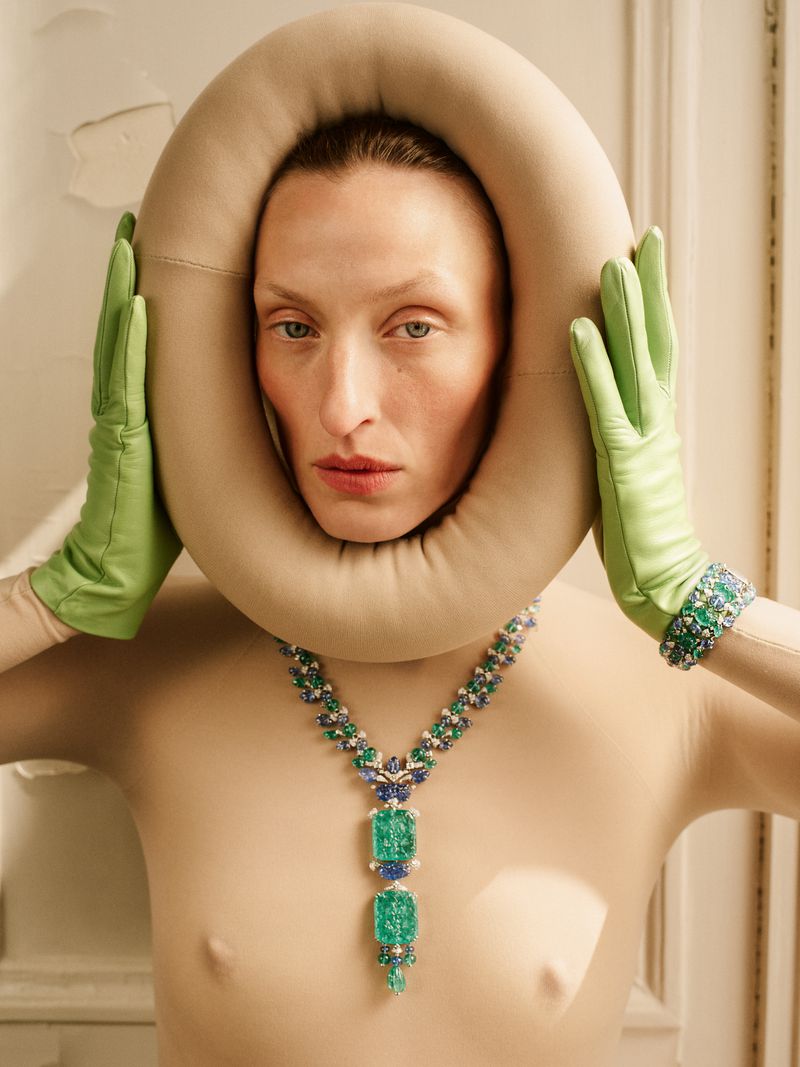 Elegant portrait of an adult female model wearing emerald jewelry, a beige collar, and lime green gloves indoors with soft lighting.