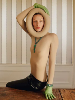 Model Maggie Maurer posing with a round sculptural neckpiece, green gloves, and a jewel necklace for Vogue Czechoslovakia
