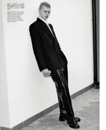 Model posing in a black double-breasted jacket and thigh-high leather boots against a white wall in black and white.