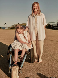 A woman and child are standing outside on a lawn bowling green. The child is in a wheelchair, and the woman stands behind her.