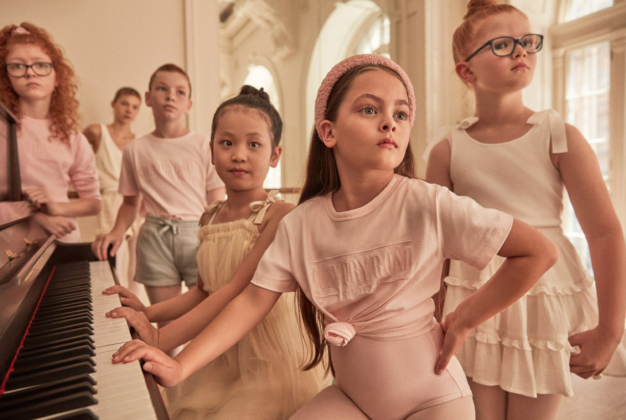 Group of children gathered around an upright piano in an ornate room for the Live With Us project by Justin Woo.