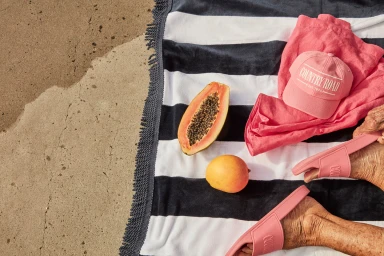 Overhead flat lay of pink slides, cap, papaya, mango, and pink towel on concrete
