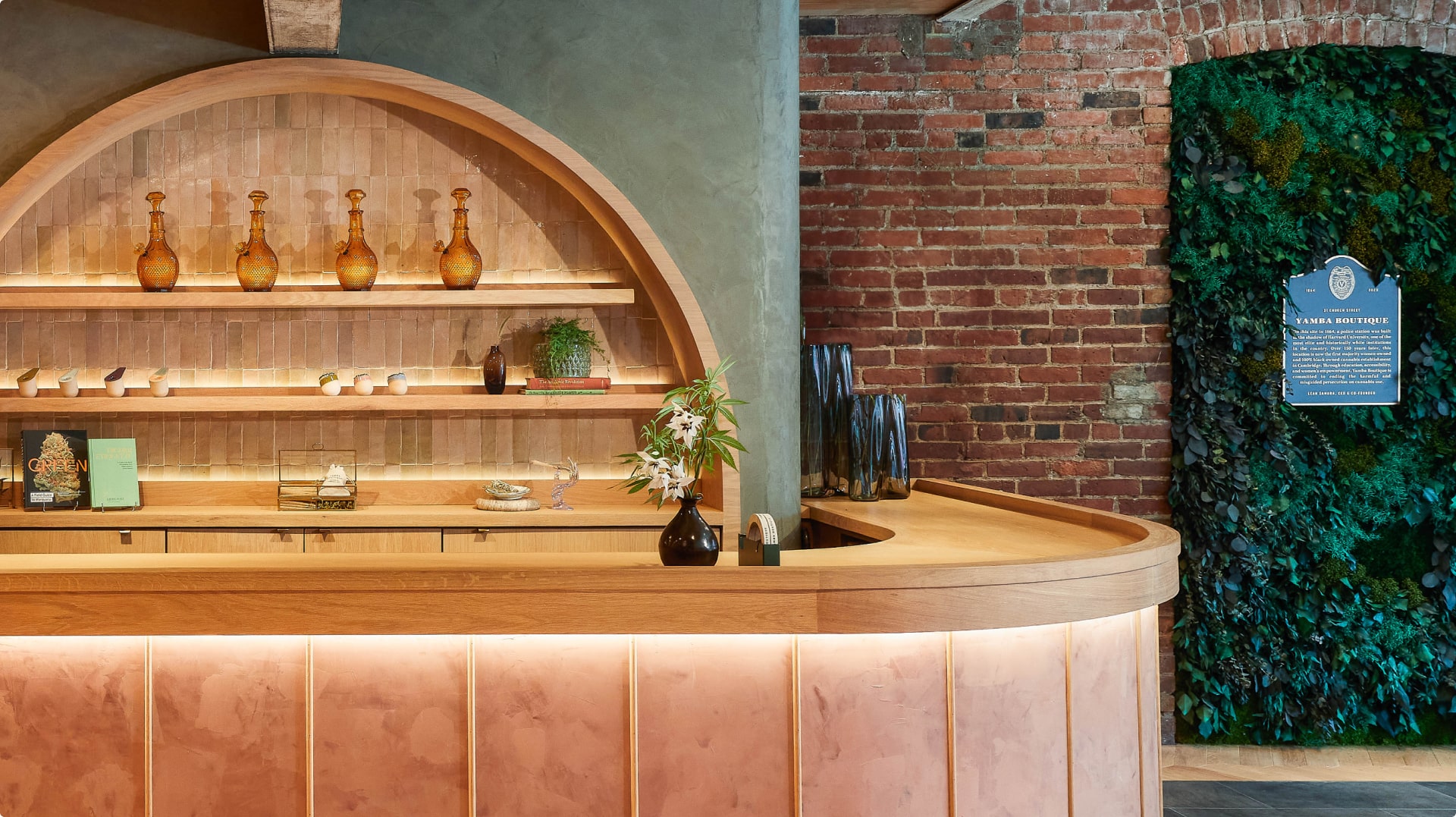 Interior view of a boutique featuring a counter with shelves displaying decorative bottles, complemented by a green wall and brick details.