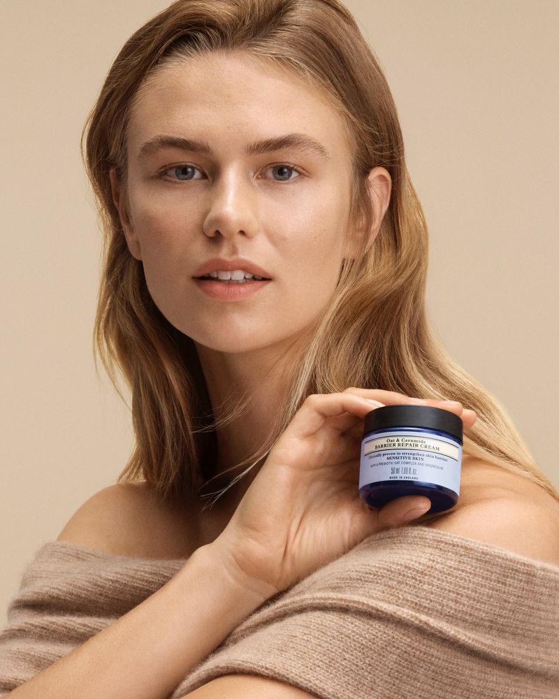 Woman in sweater holding jar of face cream in a studio shot for beauty product advertisement, showcasing skincare and complexion.