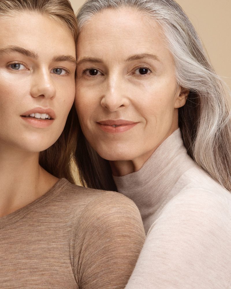 Close-up portrait of a young adult and older adult woman, both fair-skinned, with neutral expressions in front of a beige background.