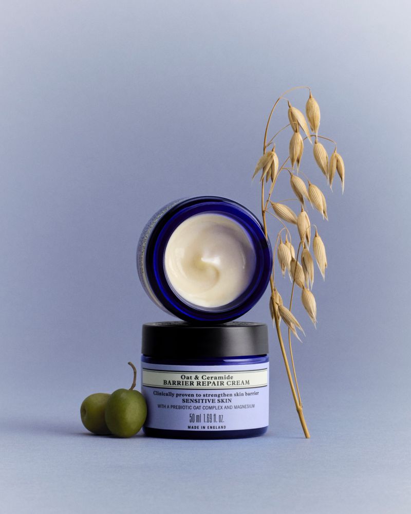 Stacked skincare jars with oats and olives on a blue background, studio shot for the beauty and wellness industry.