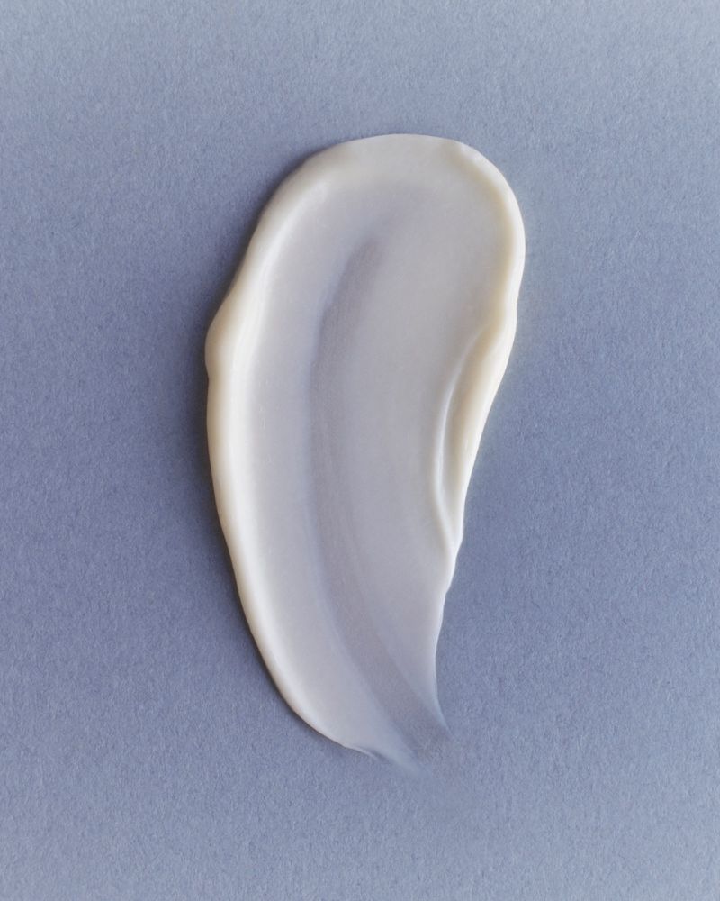 Close-up of a thick, light-colored cosmetic cream swatch against a solid light blue-gray background, ideal for beauty and skincare promotions.