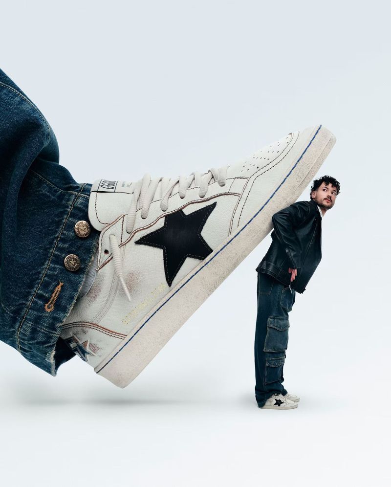 Low-angle shot of an adult male appearing to hold up a large, worn-looking sneaker with a black star against a white backdrop.