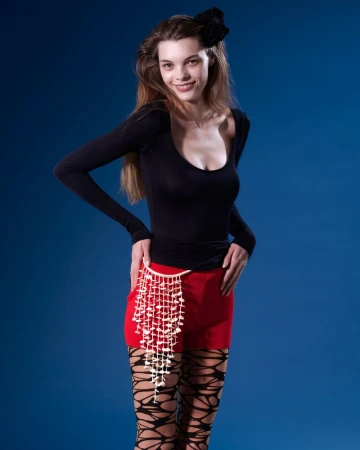 Studio shot of a young adult woman wearing a long-sleeved black top, red skirt, patterned stockings, and a decorative waist chain. 