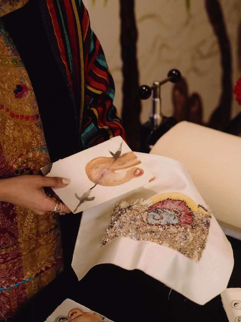 Artisan displays mixed-media textile art; watercolor sketch and textured fabric, showcased on white cloth in an indoor setting.
