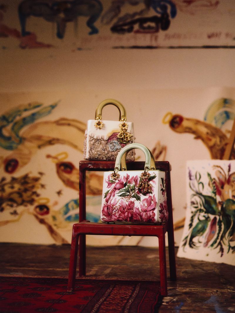 Two Lady Dior handbags with floral and beaded decoration on a red stool in front of a painted wall, luxury fashion accessories.