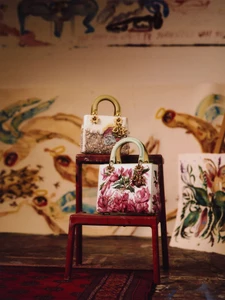 Two embroidered Dior Lady Art project handbags arranged on a red wooden step stool in an artist studio setting.