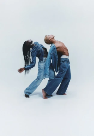 Two models in denim, a black woman and a light-skinned man, are in a studio with a white background, fashion shot, stylish and creative.