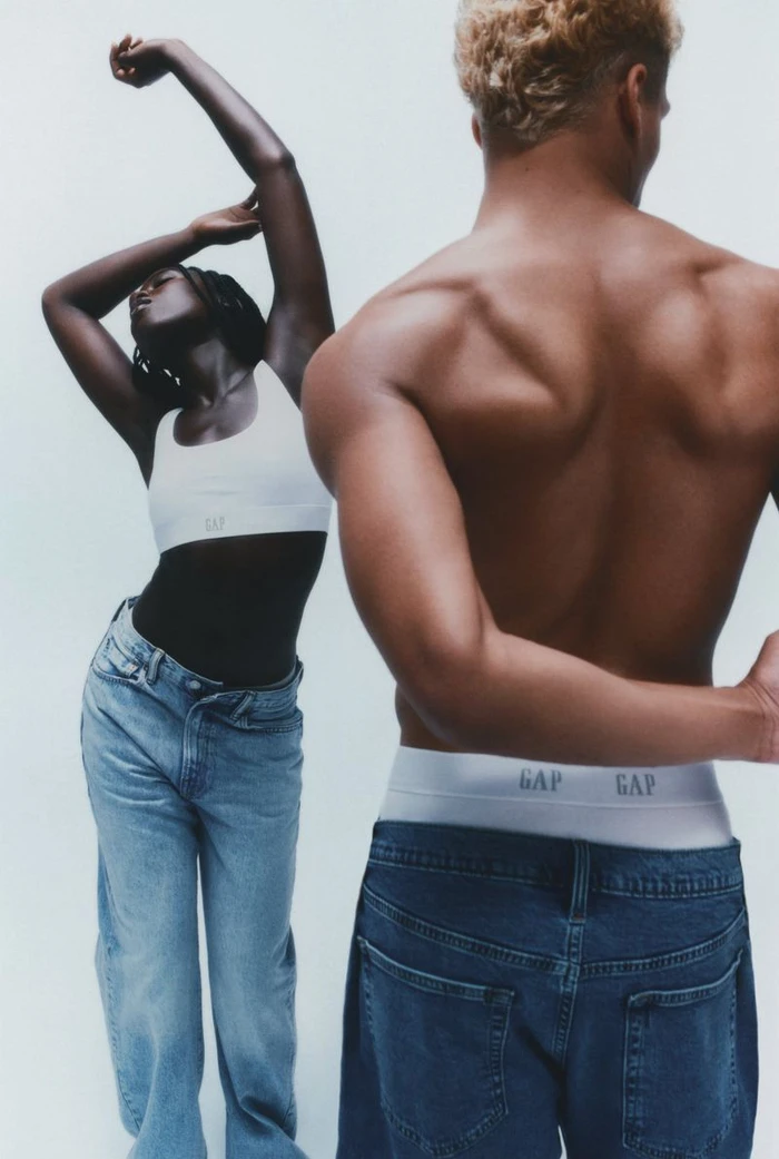 A shirtless man with blonde hair and a woman in a white bralette and blue jeans posing against a white background for Gap