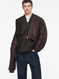 Male model in a textured tweed blazer, draped brown bomber jacket, and dark blue jeans against a white seamless background.