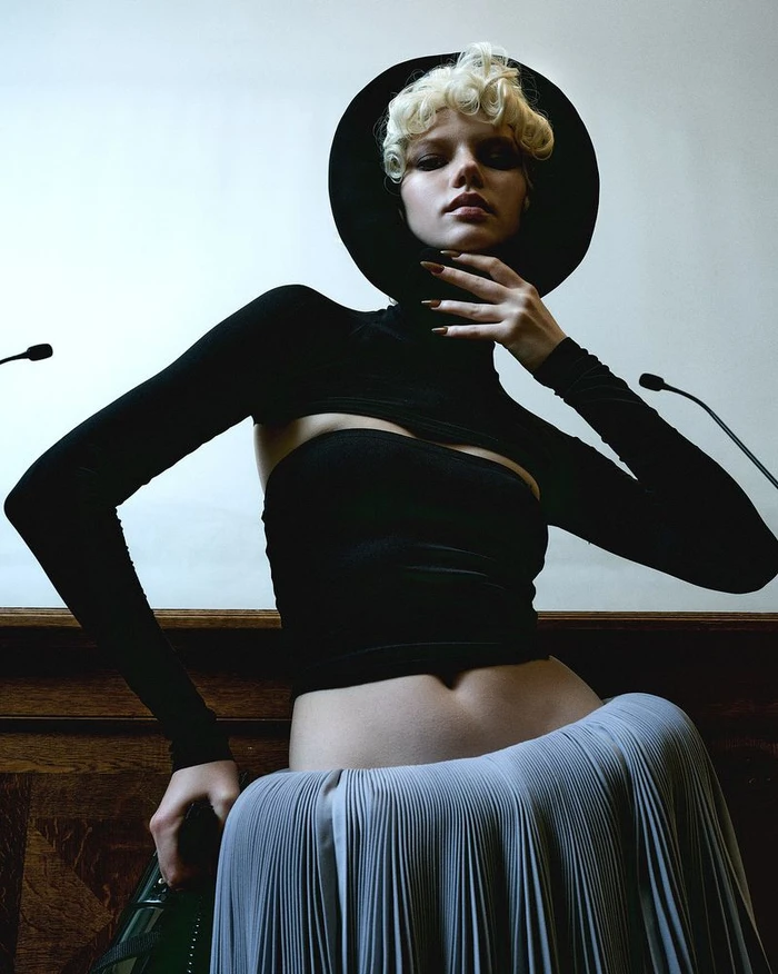 Model Olga Lane wearing a black cut-out top, round black headpiece, and pleated grey skirt for Numéro France.