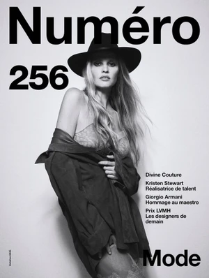 Black and white magazine cover featuring a blonde model wearing a wide-brim hat and an unbuttoned jacket over lace lingerie.