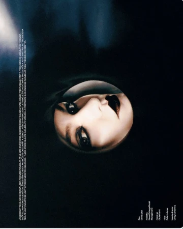 Fashion magazine cover with portrait of a pale-skinned adult female with heavy makeup, dark lipstick, and a shadowy black background.