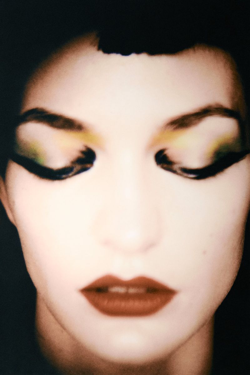 Close-up beauty portrait of a woman with closed eyes featuring dramatic graphic black eyeliner, yellow eyeshadow, and dark red lipstick.