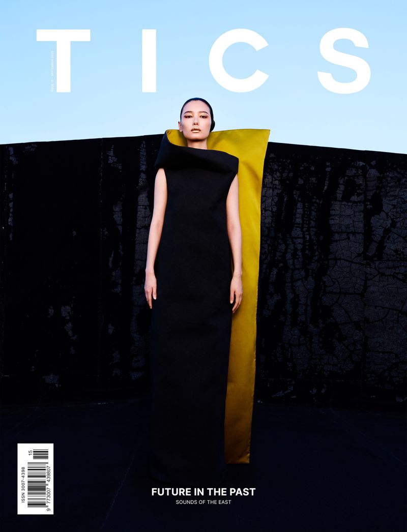 Magazine cover featuring a woman in a black dress with a striking yellow element, against a backdrop of black texture and light blue sky.