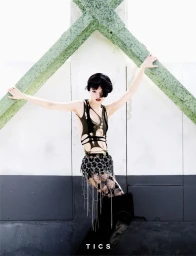 Model in cutout top and fringed skirt posing against architectural crossbeams for TICS Magazine