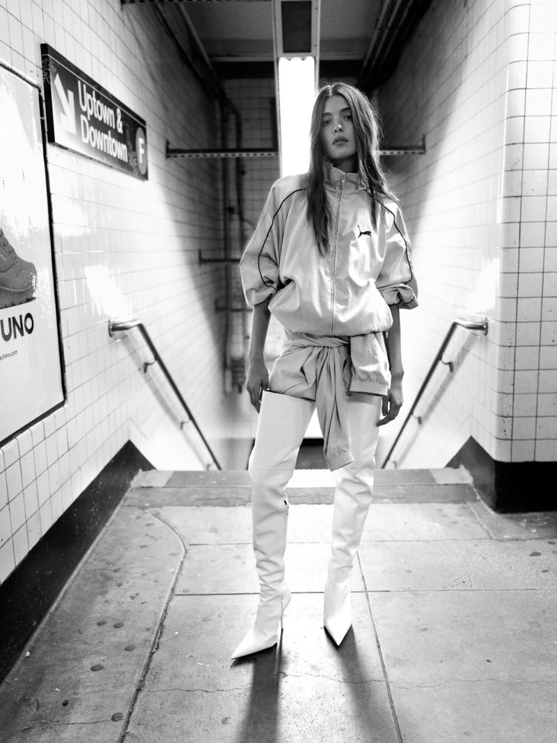 Woman in a tracksuit and thigh-high boots poses on steps in a subway. Black and white fashion shot in an urban environment.