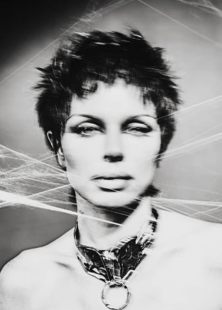 Monochrome portrait of a person with short spiky hair and a large metal necklace, styled with a web-like effect. Fashionable, striking.