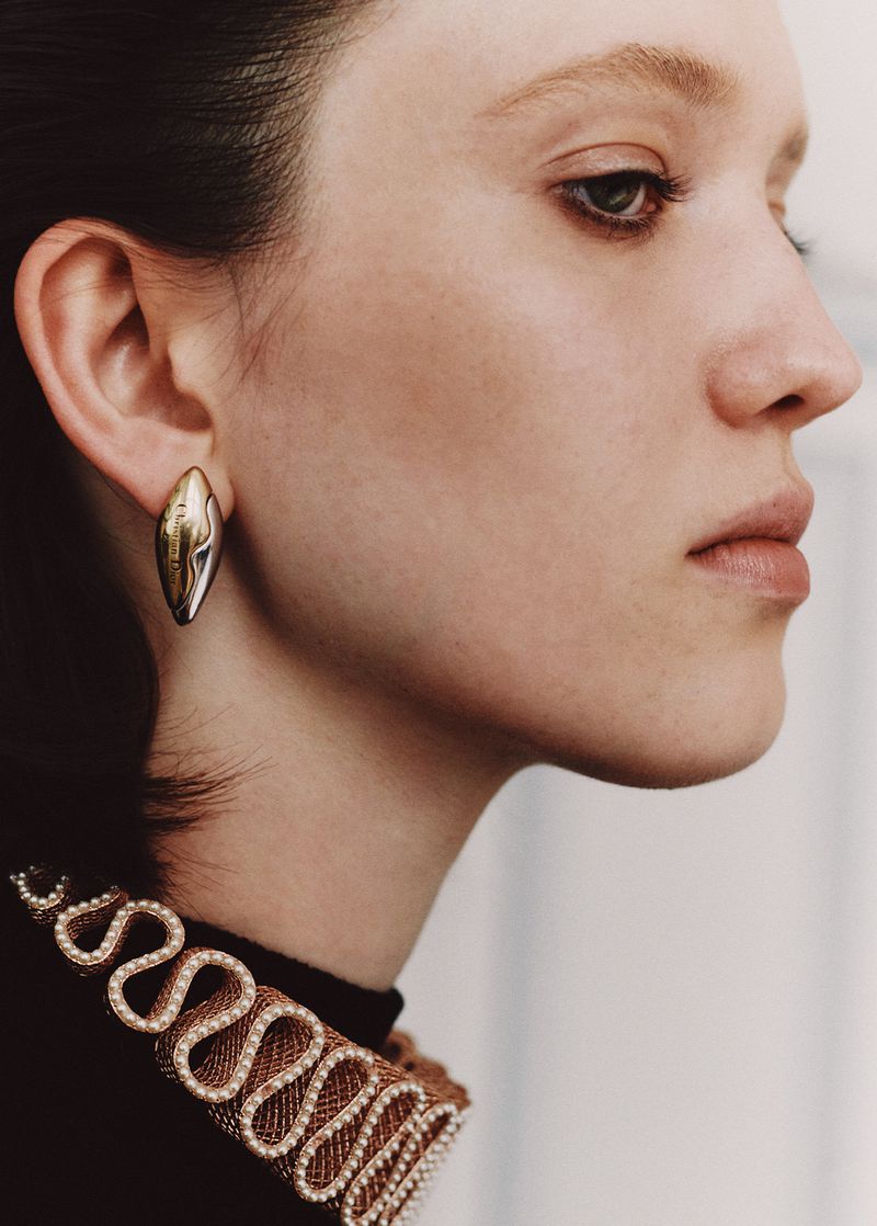 Close-up profile of a woman with fair skin, wearing a gold earring and a black top with a decorative neckline.