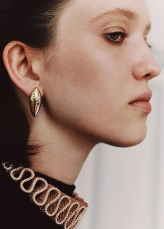 Close-up profile of a woman with fair skin, wearing a gold earring and a black top with a decorative neckline.
