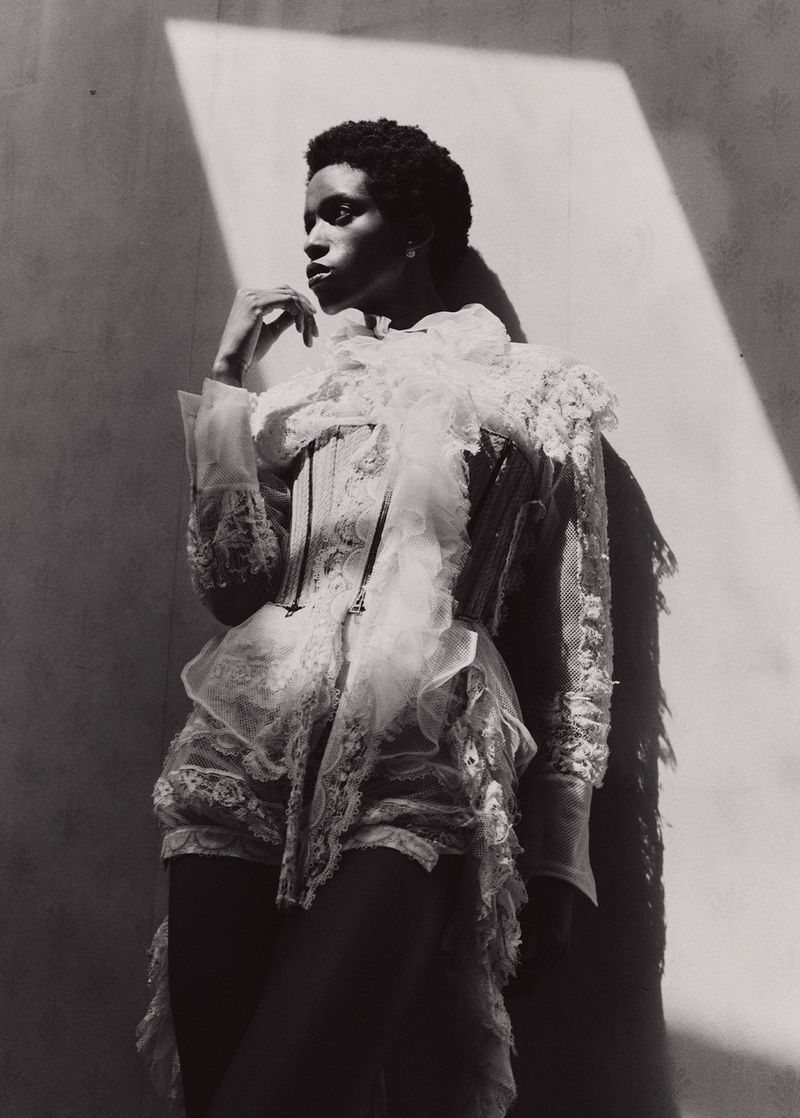 Black and white portrait of a person wearing a lace ruffled top and corset in a photo studio with sunlight, fashion photography.